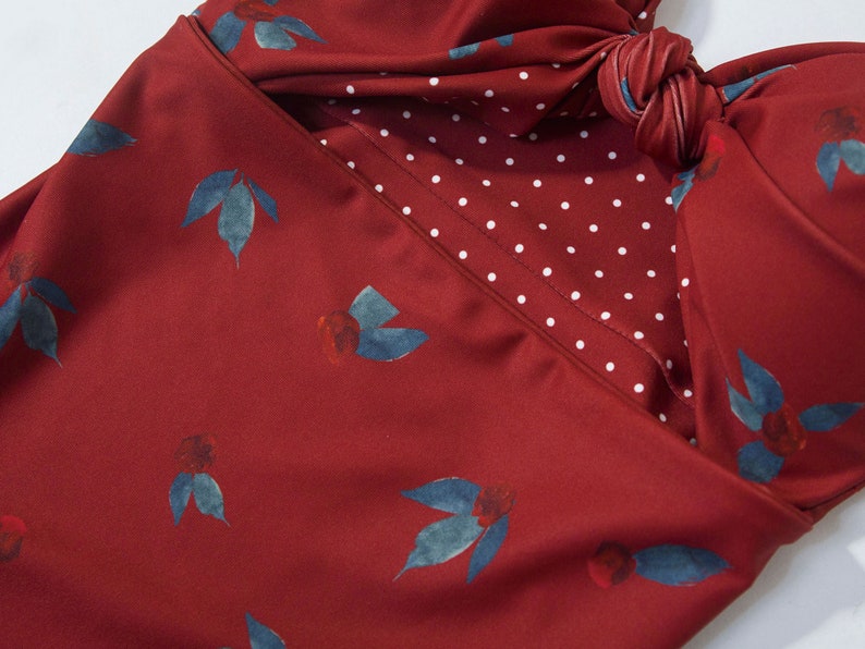 May include: A red swimsuit with a white polka dot pattern on the inside. The swimsuit has a knotted detail at the top and a floral print.
