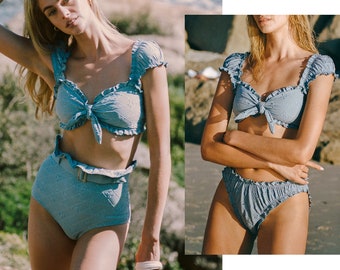 May include: A light blue bikini with a ruffled top and high-waisted bottoms. The top has a tie at the front and the bottoms have a belt.