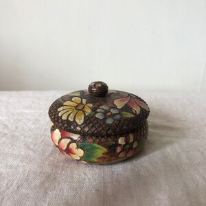 Könnte beinhalten: Eine kleine Holzkiste mit einem floralen Design, das auf Deckel und Seiten gemalt ist. Die Kiste ist in Braun-, Gelb-, Rosa-, Grün- und Blautönen bemalt.