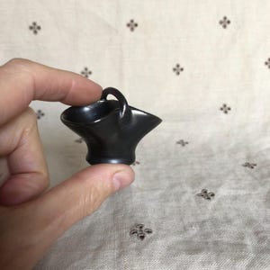 Peut inclure: Un petit panier en céramique noire avec une anse. Le panier a une forme évasée et une finition lisse et brillante. Le panier est tenu dans la main d'une personne.