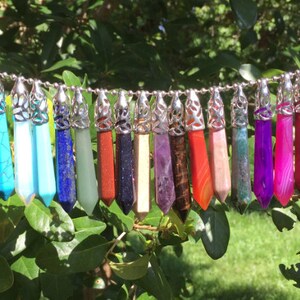 May include: A string of 18 crystal point pendants with silver-tone metal caps. The pendants are in various colors, including pink, turquoise, blue, green, red, purple, and white.