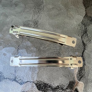 May include: Two silver metal hair clips. The clips are about 4 inches long and have a smooth, shiny finish.