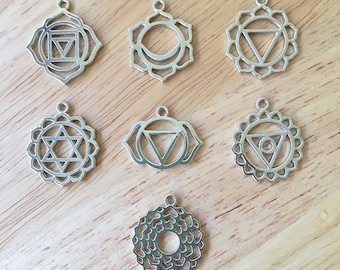 May include: Seven silver metal charms with different chakra symbols. Each charm is a circular design with a different symbol in the center. The symbols are the root chakra, sacral chakra, solar plexus chakra, heart chakra, throat chakra, third eye chakra, and crown chakra.