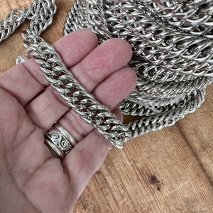 May include: A silver curb chain necklace with a thick, chunky design. The chain is shown in a hand, highlighting its size and weight.