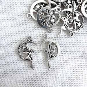 May include: Silver-toned metal charms featuring a crescent moon design with stars and a fairy silhouette. The charms have a loop at the top for easy attachment. Ideal for jewelry making or crafting projects.