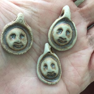 May include: Three ceramic pendants with a brown glaze and a white background. Each pendant features a simple face with a smile.