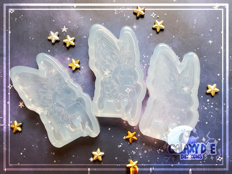 May include: Three clear silicone molds of fairies with wings, sitting on a mushroom. The molds are on a dark blue background with gold stars.