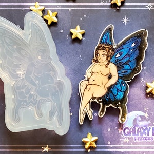 May include: A clear silicone mold of a fairy with blue wings. The fairy is sitting with its legs crossed and has a large, round body. The mold is on a dark blue background with gold stars.