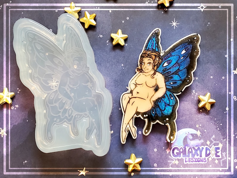 May include: A clear silicone mold of a fairy with blue wings. The fairy is sitting with its legs crossed and has a large, round body. The mold is on a dark blue background with gold stars.