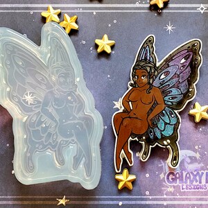 May include: A silicone mold of a fairy with wings, sitting on a throne. The fairy has a detailed face and body, and the wings are intricate and detailed. The mold is clear and translucent.