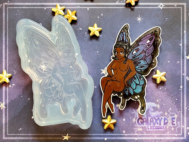 May include: A silicone mold of a fairy with wings, sitting on a throne. The fairy has a detailed face and body, and the wings are intricate and detailed. The mold is clear and translucent.