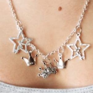 May include: Silver-toned necklace featuring star and crown charms. The necklace has a delicate chain and multiple charms, including openwork stars and small crown pendants. The jewelry is worn around the neck.