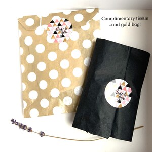 May include: Two paper bags, one tan with white polka dots and one black, are shown. Each bag has a round sticker with a geometric design and the words "thank you." The text "Complimentary tissue...and gold bag!" is also visible.
