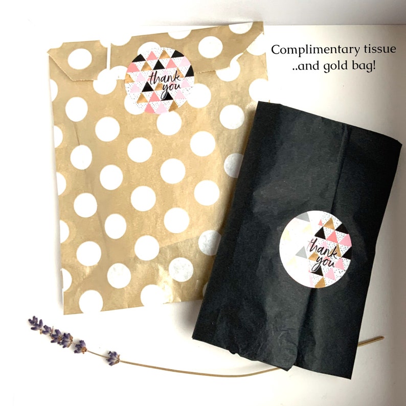 May include: Two paper bags, one tan with white polka dots and one black, are shown. Each bag has a round sticker with a geometric design and the words "thank you." The text "Complimentary tissue...and gold bag!" is also visible.