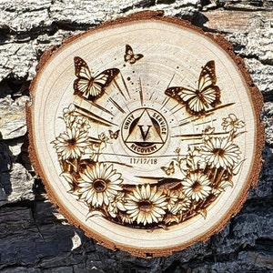 Puede incluir: Un círculo de madera con un diseño quemado de un triángulo con las palabras "Unidad, Servicio, Recuperación" y la letra "V" en su interior. El círculo está rodeado por un diseño de flores y mariposas. La fecha "11/17/18" también está quemada en la madera.