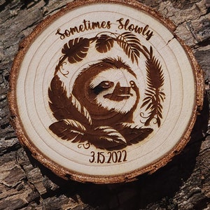 May include: A wooden round slice with a sloth design and the text "Sometimes slowly" and the date "3.15.2022".