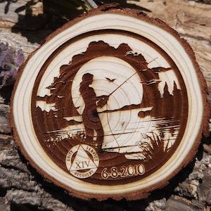 May include: A wooden circle with a silhouette of a person fishing in a lake. The circle has a triangle with the words "Unity", "Service", and "Recovery" and the number "XIV" inside. The date "6-8-2010" is also engraved on the circle.