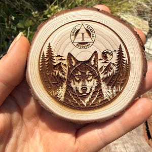 May include: A circular wood slice featuring a laser-engraved design of a wolf centered in front of a mountain and forest landscape. Above the wolf is a triangle emblem containing the Roman numeral I and the words Unity, Service, and Recovery.