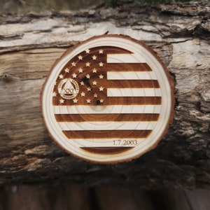 May include: A wooden round disc with a burned-in image of the American flag. The flag has 13 stripes and 50 stars. The disc also has a circle with the words "Unity, Service, Recovery" and the number "XXI" inside. The date "1.7.2003" is also burned into the disc.