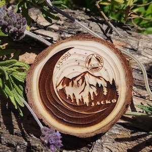 May include: A round wooden coaster with a mountain and forest design, engraved with the date 3.15.1995 and the name JACKO. The coaster also features the text "UNITY SERVICE RECOVERY" and a symbol.