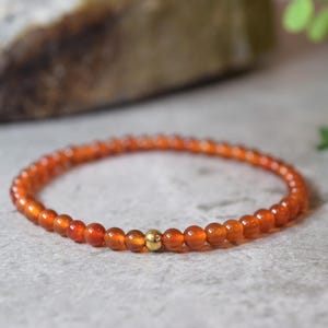 May include: A carnelian gemstone bracelet with a gold bead accent. The bracelet is made of small, round beads and is a light orange colour.