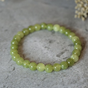May include: A bracelet made of light green, spherical beads. The beads are strung together to form a circular band. The gemstones have a polished, glossy finish and a consistent, pale green colour. The bracelet is a piece of jewellery.