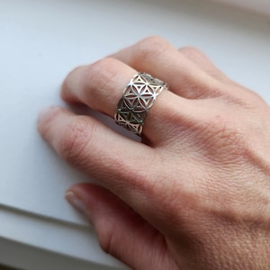 May include: A silver ring featuring a geometric design, reminiscent of a flower of life pattern.