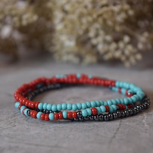 May include: Three beaded bracelets in red, turquoise, and black. The bracelets are stacked on top of each other.