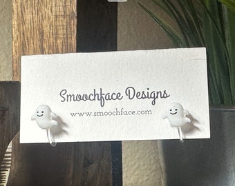 May include: A pair of white ghost earrings with a smiling face. The earrings are on a white card with the text "Smoochface Designs" and "www.smoochface.com".