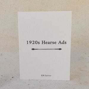May include: A white card with the text "1920s Hearse Ads" in black, centered above a decorative line. The author's name, "KM Sarver," is printed at the bottom. The card is on a neutral-toned fabric surface.