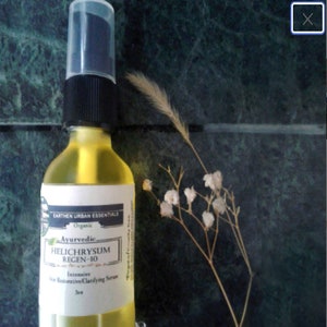 Puede incluir: Una botella de vidrio transparente con un l&iacute;quido amarillo en su interior. La botella tiene una tapa negra y una etiqueta blanca que dice "EARTHEN URBAN ESSENTIALS Organic Ayurvedic HELICHRYSUM REGEN-10 Intensive Skin Restorative Clarifying Serum 30ml".