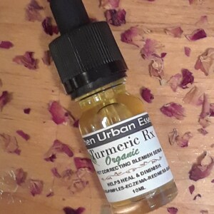 Pode incluir: Um pequeno frasco de vidro transparente com um conta-gotas preto. O frasco &eacute; etiquetado com "Turmeric Rx Organic Spot Correcting Blemish Serum" e "Helps Heal & Diminish Pimples-Eczema-Redness of 10ML".