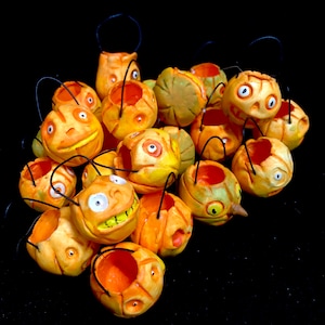 Puede incluir: Un grupo de 15 pequeños cubos de calabaza de cerámica naranja y amarilla con asas negras. Cada calabaza tiene una cara pintada diferente.