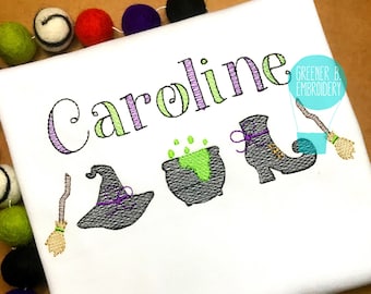 May include: Embroidered design featuring the name "Caroline" in green and purple lettering, with a witch's hat, cauldron, boot, and broom. The design is on a white t-shirt.