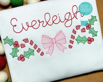 May include: White fabric with red embroidered text "Everleigh", a pink bow, candy canes, and holly leaves. The design includes the text "Greener B. Embroidery". Festive, holiday-themed apparel.