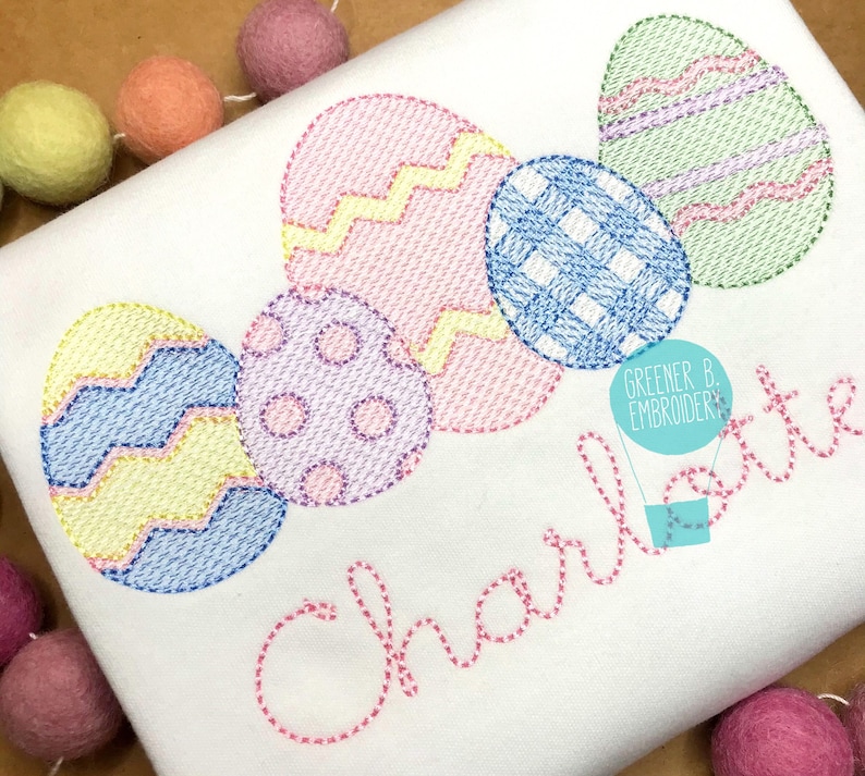 May include: A white t-shirt with embroidered pastel colored Easter eggs and the name "Charlotte" in pink thread. The text "Greener B. Embroidery" is also embroidered in blue thread.