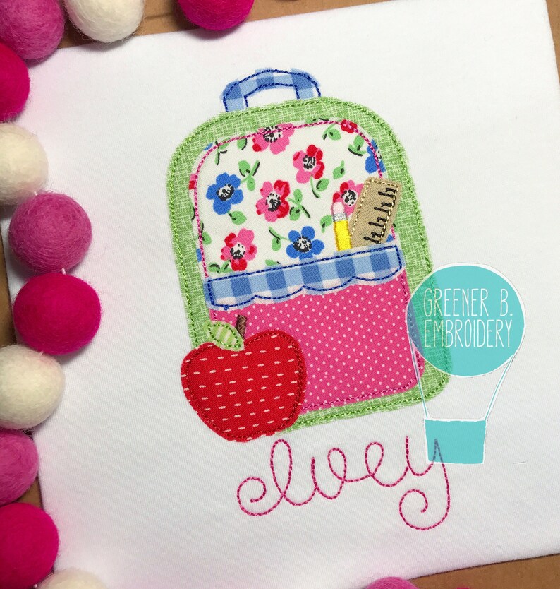 May include: A green and pink backpack with a red apple and a pencil in the pocket. The backpack has a floral pattern and the name "elvey" is embroidered below it.