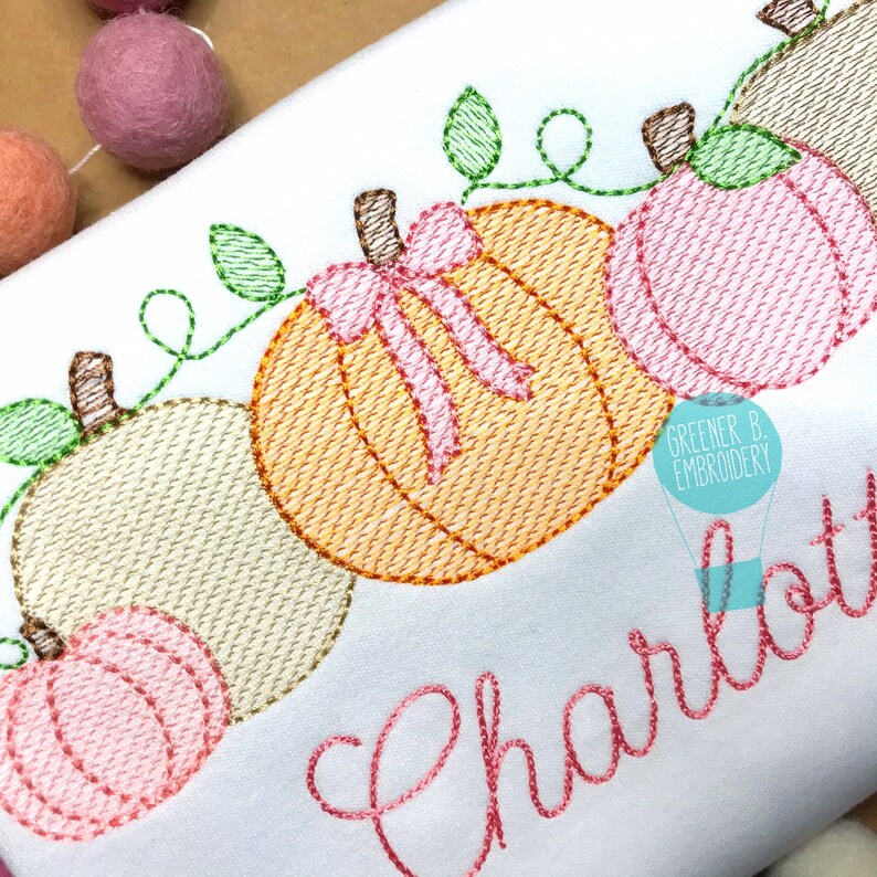 Peut inclure: Broderie repr&eacute;sentant une rang&eacute;e de citrouilles avec des vignes vertes et un n&oelig;ud rose sur une citrouille. Le nom "Charlotte" est brod&eacute; sous les citrouilles.