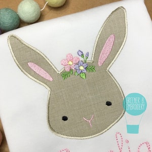 May include: Embroidered bunny head with a floral crown in shades of pink, purple, and green. The bunny has a brown face with black eyes and a pink nose. The text "Greener B. Embroidery" is visible in the bottom right corner.