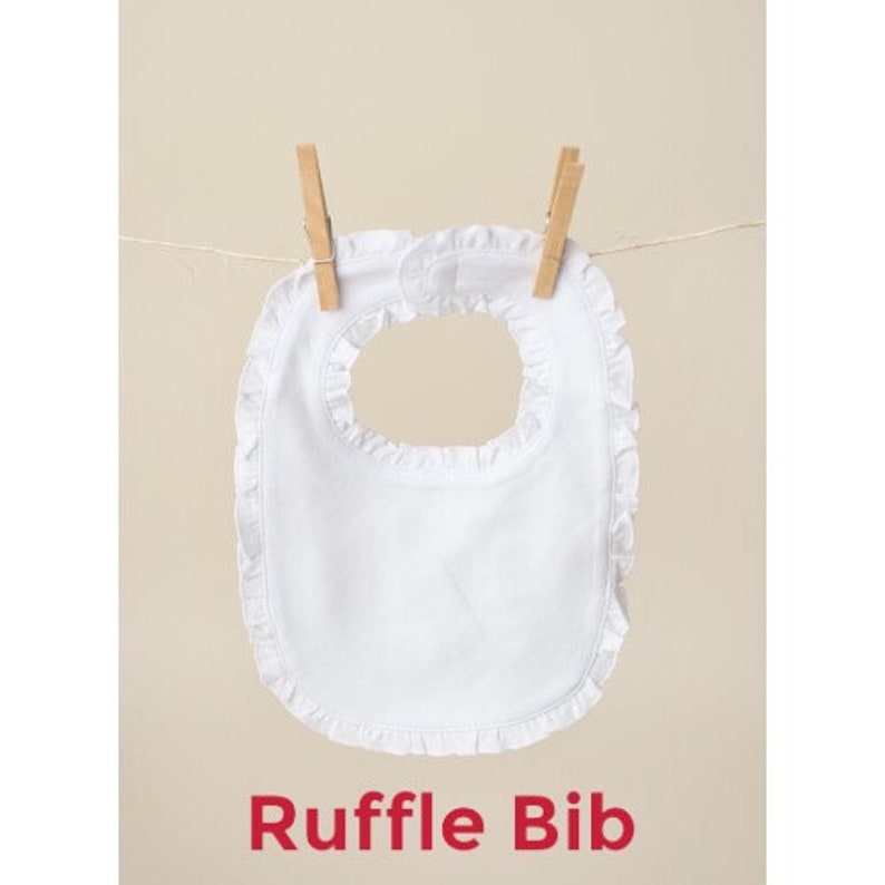 May include: White cotton baby bib with a ruffled edge. The bib is hanging on a clothesline with wooden clothespins. The text "Ruffle Bib" is printed below the bib.