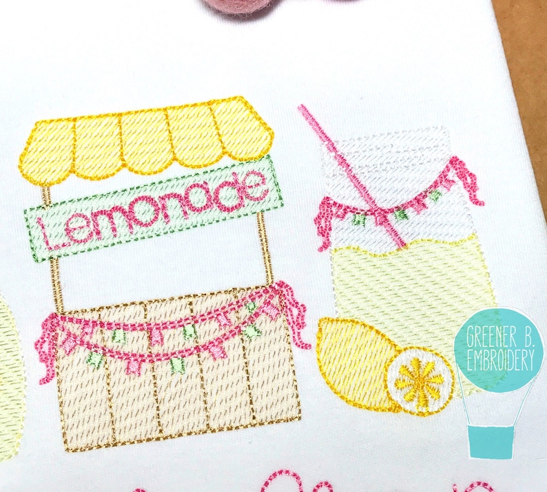 Puede incluir: Dise&ntilde;o bordado de un puesto de limonada con un toldo amarillo, una caja de madera y una guirnalda rosa y verde. Un vaso de limonada con una pajita y una rodaja de lim&oacute;n est&aacute; al lado del puesto.