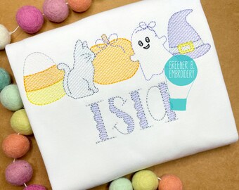 May include: A white t-shirt with purple embroidery of a candy corn, a cat, a pumpkin, a ghost, a witch's hat, and the name "Isla". The embroidery is stitched in a simple, hand-drawn style. The text "Greener B. Embroidery" is also embroidered in purple on the shirt.