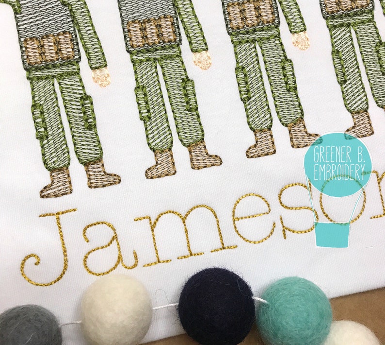 Puede incluir: Dise&ntilde;o bordado de cinco soldados con uniformes verdes y marrones con el nombre Jameson en letras doradas debajo. El dise&ntilde;o est&aacute; sobre un fondo de tela blanca.