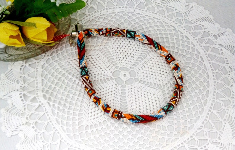 May include: A colorful beaded necklace with a geometric pattern in shades of red, orange, blue, and white. The necklace is made of small beads and has a silver clasp.