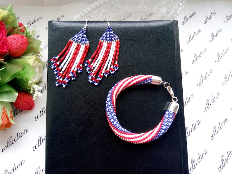 Peut inclure: Un ensemble de bijoux en perles de couleur rouge, blanc et bleu. L'ensemble comprend un bracelet et une paire de boucles d'oreilles pendantes. Les bijoux sont faits de petites perles et ont un th&egrave;me patriotique.
