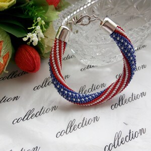 Peut inclure: Un bracelet en perles avec des perles rouges, blanches et bleues dispos&eacute;es en un motif ressemblant au drapeau am&eacute;ricain.
