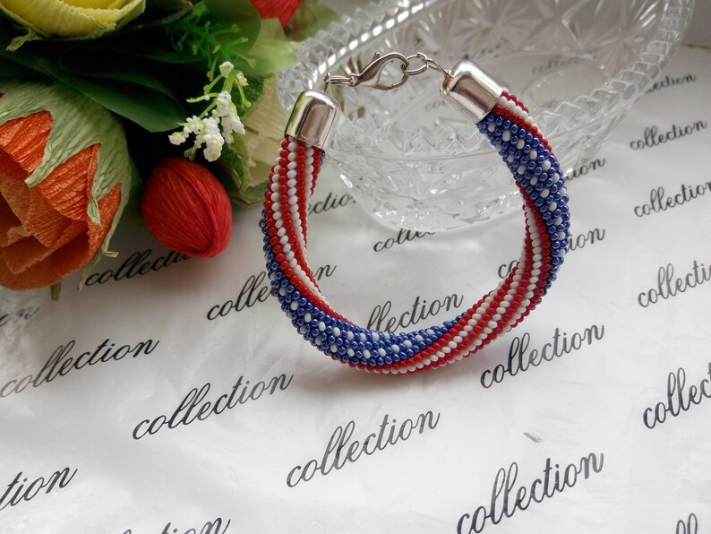 Peut inclure: Un bracelet en perles avec des perles rouges, blanches et bleues dispos&eacute;es en un motif ressemblant au drapeau am&eacute;ricain.