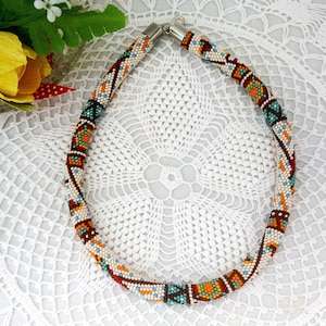 May include: A colorful beaded necklace with a geometric pattern in shades of brown, orange, white, and blue. The necklace is made of small beads and has a silver clasp.