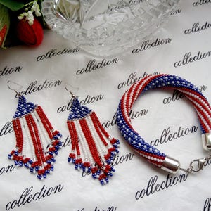 Peut inclure: Un ensemble de bijoux en perles comprenant un bracelet et des boucles d'oreilles. Le bracelet et les boucles d'oreilles sont faits de perles rouges, blanches et bleues dans un motif qui ressemble au drapeau am&eacute;ricain.