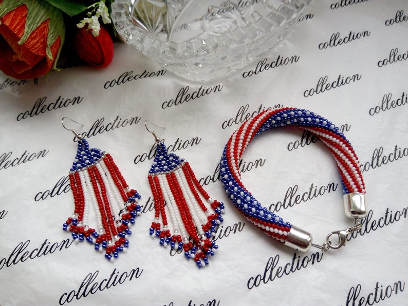Peut inclure: Un ensemble de bijoux en perles comprenant un bracelet et des boucles d'oreilles. Le bracelet et les boucles d'oreilles sont faits de perles rouges, blanches et bleues dans un motif qui ressemble au drapeau am&eacute;ricain.
